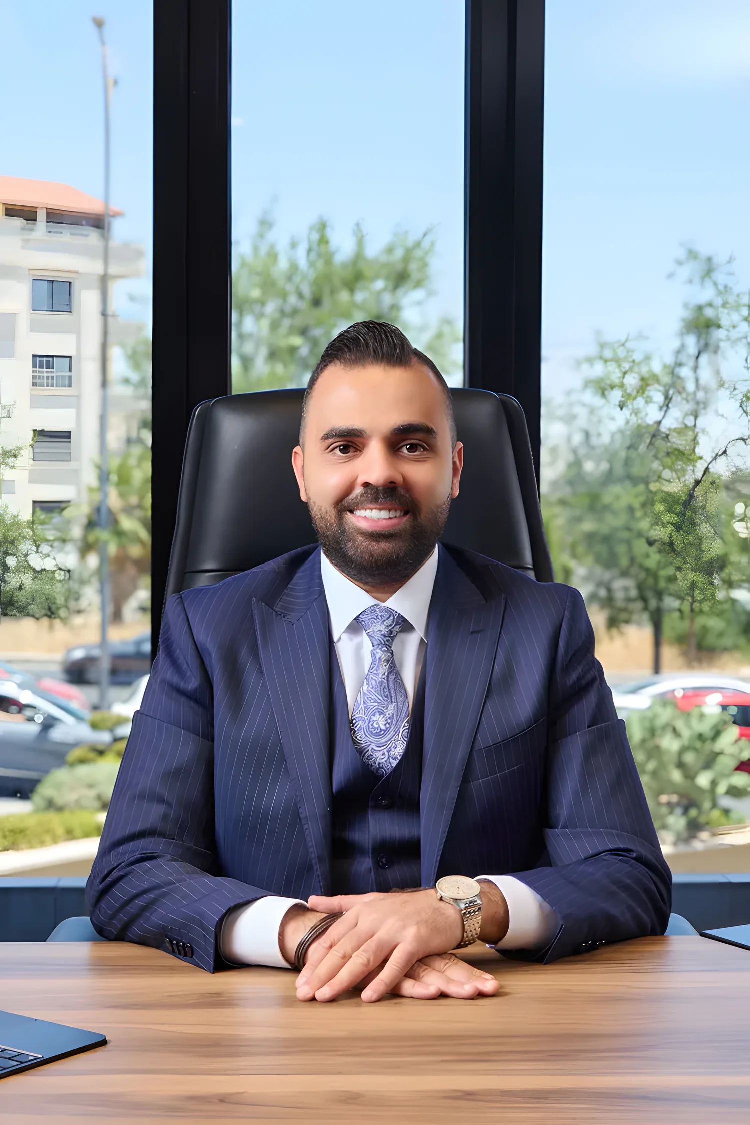 The founder and chairman of Al Kayan Hotel Investment seated at his desk in a navy pinstripe suit, hands folded, daylight and greenery behind him