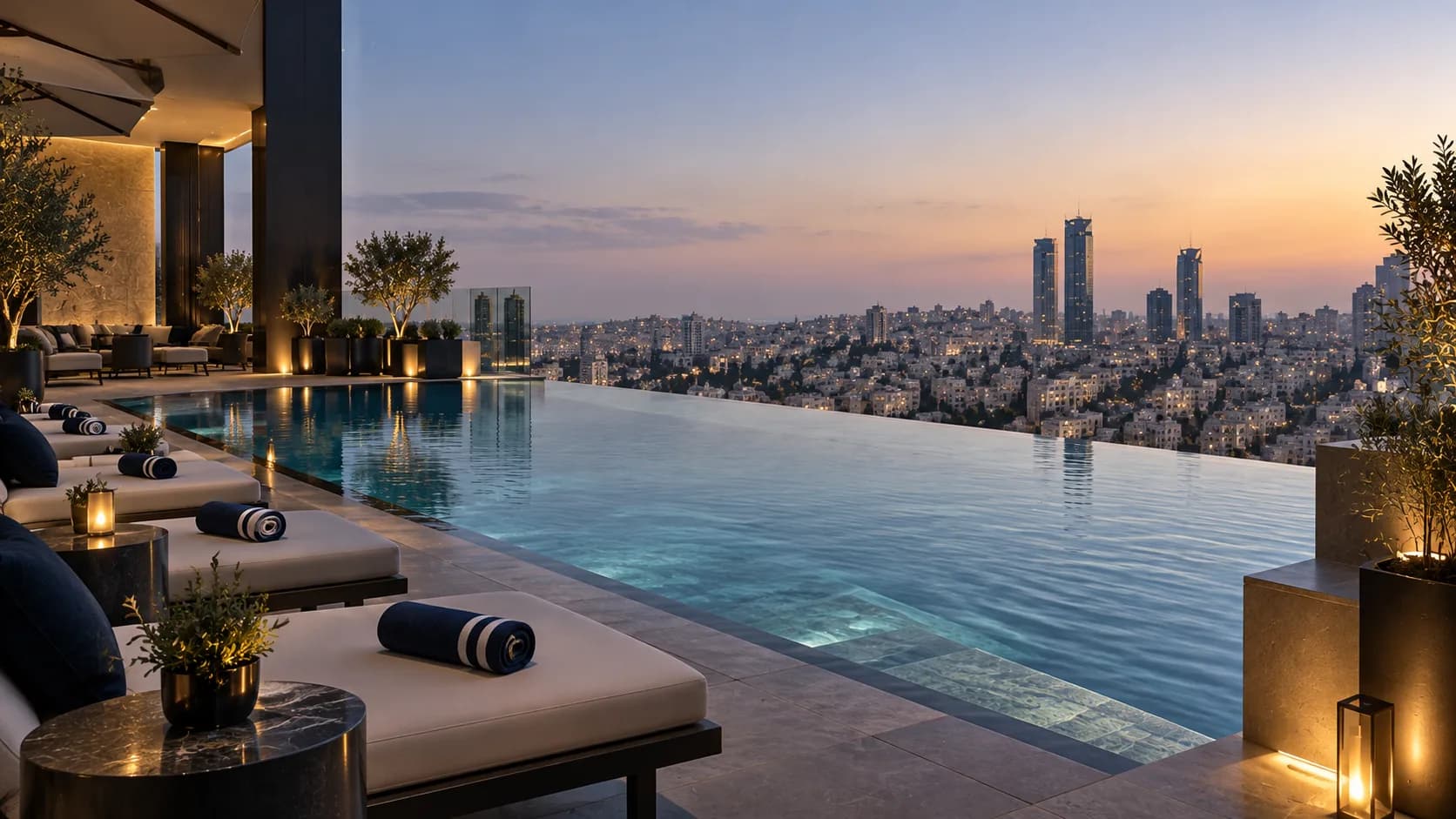 Rooftop infinity pool at sunset on the Al Kayan hotel, navy sun loungers and olive trees along the water's edge overlooking the Amman skyline